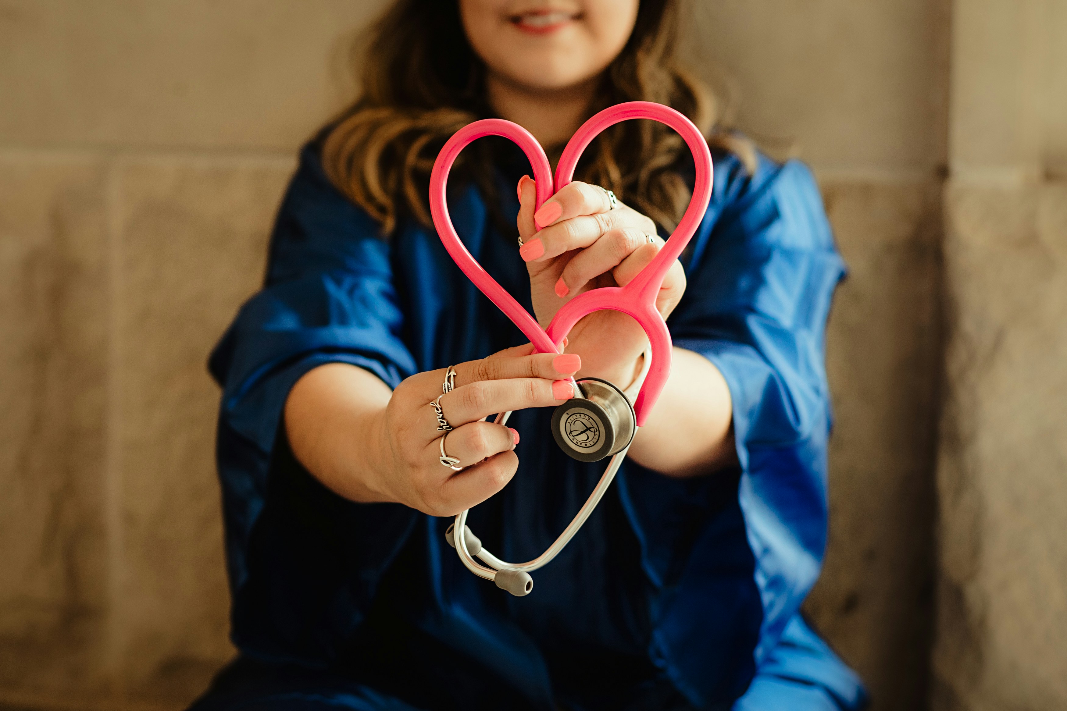 Nurse in scrubs holding a stethoscope shaped into a heart